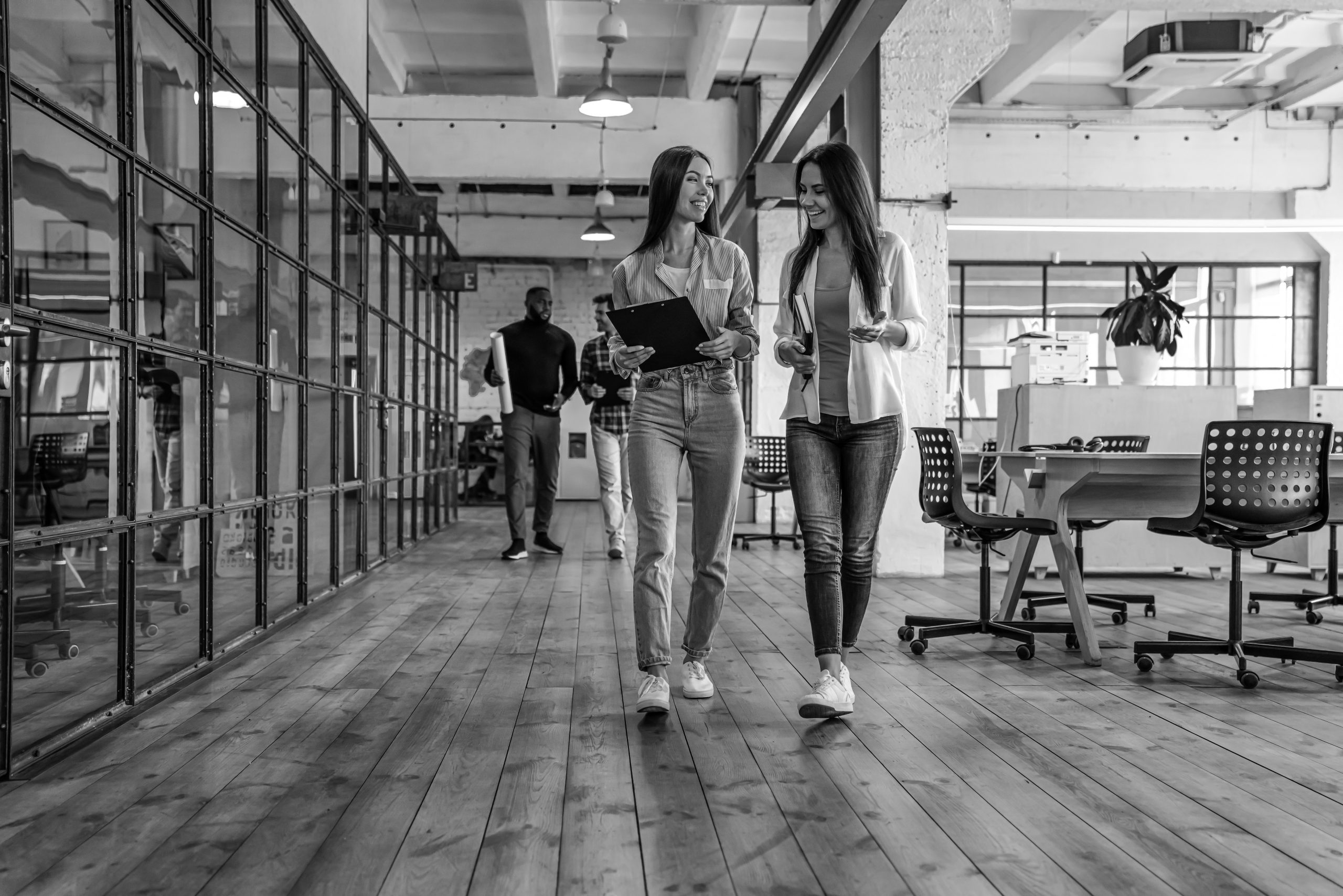 Sharing fresh office news. Two young colleagues in smart casual wear discussing business and smiling while walking through the office